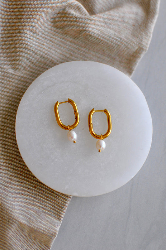 Gold hoop earrings with pearl accents on a white stone surface.
