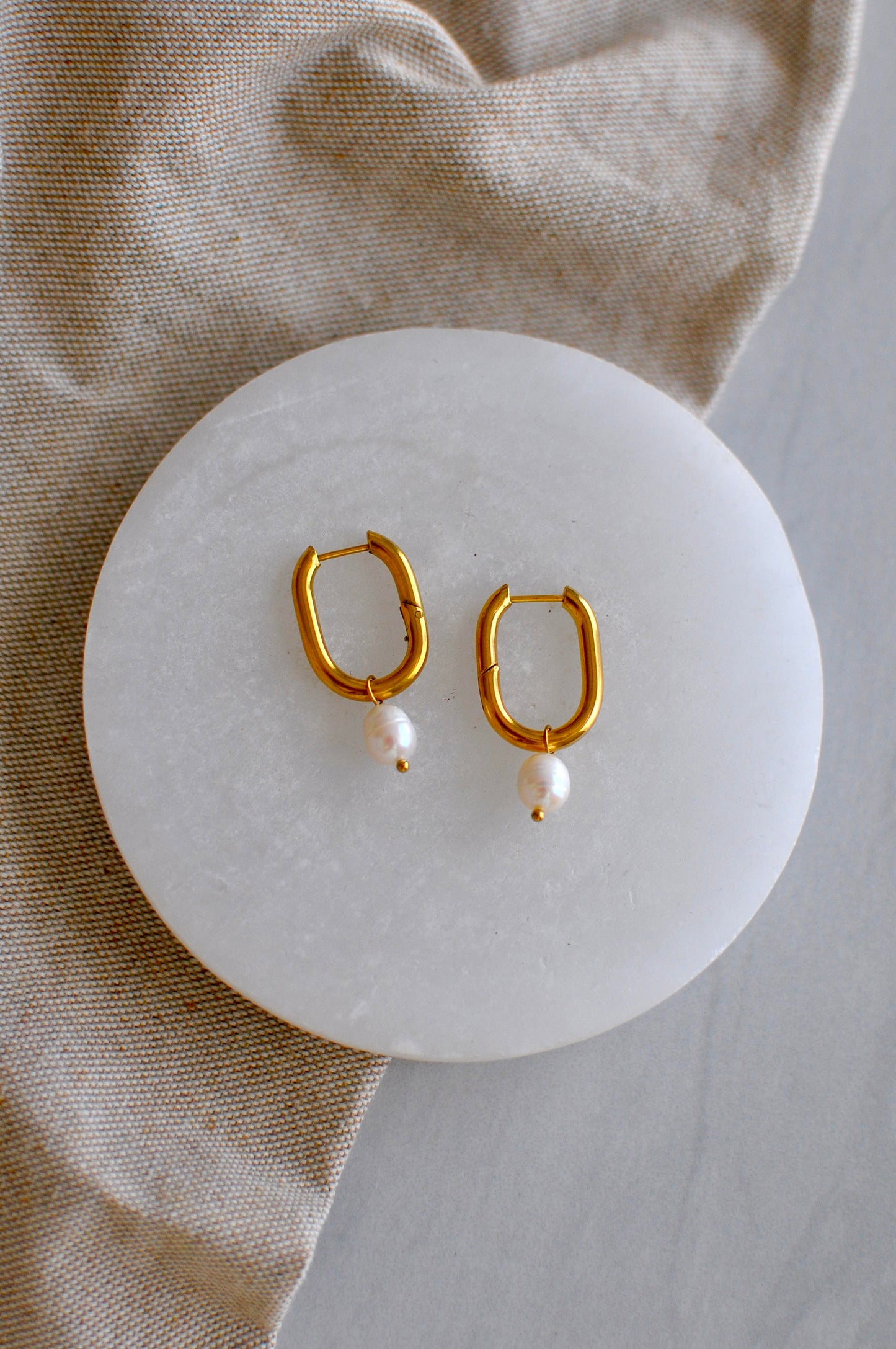 Gold hoop earrings with pearl accents on a white stone surface.