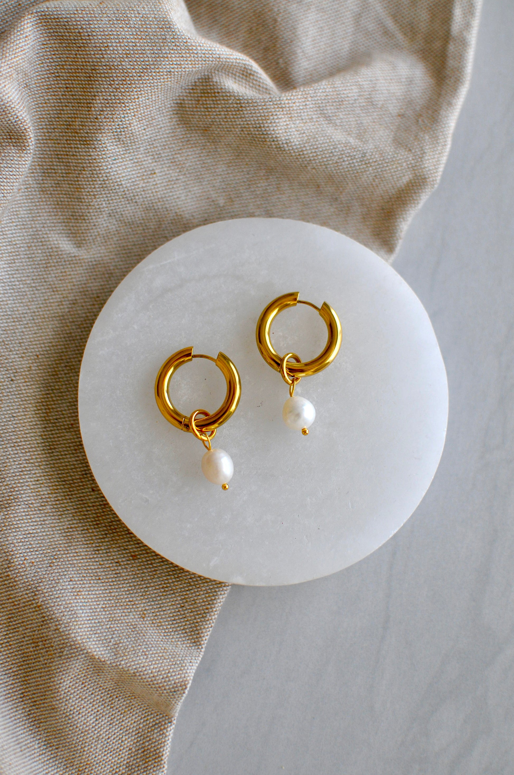 Gold hoop earrings with pearls on a white stone surface, beige fabric background